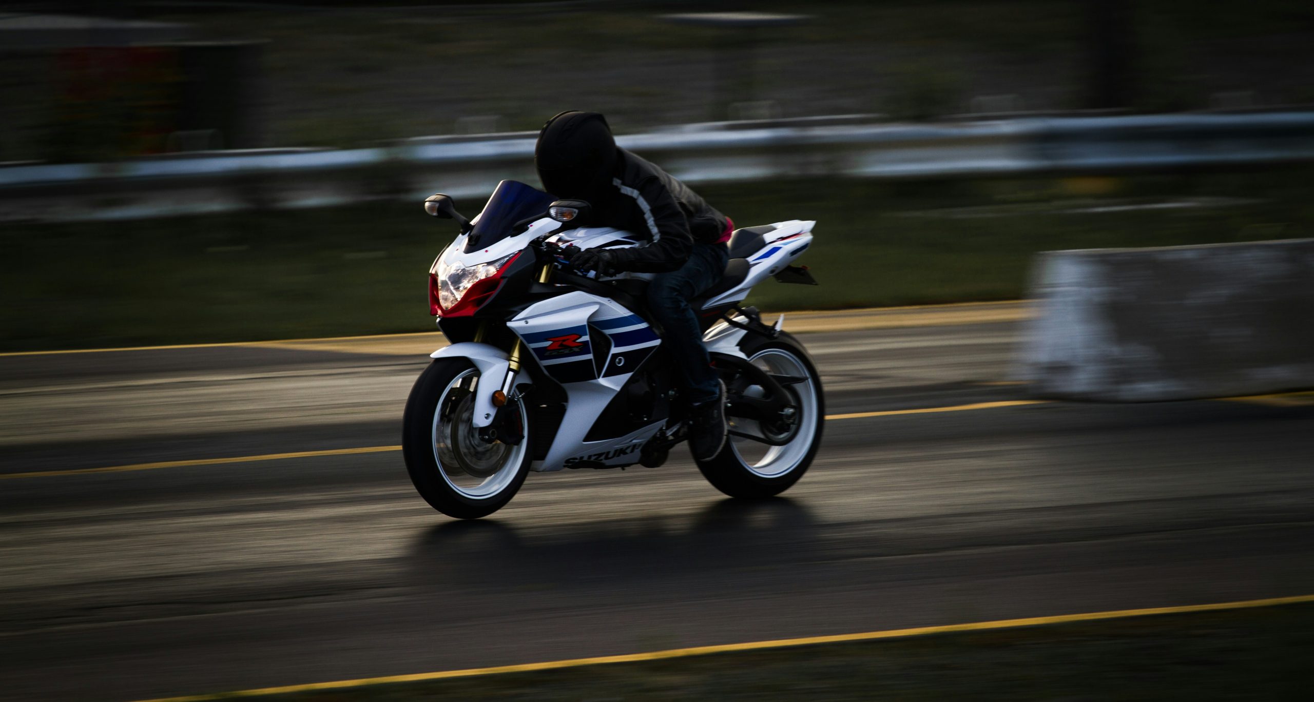 A motorcyclist in black motorcycle gear riding a white motorcycle with blured background