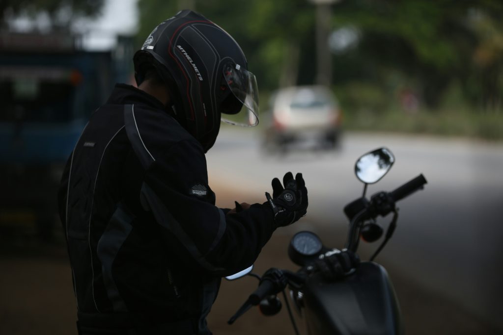 A man wearing motorcycle gear, helemt and fastening his motorcycle glove