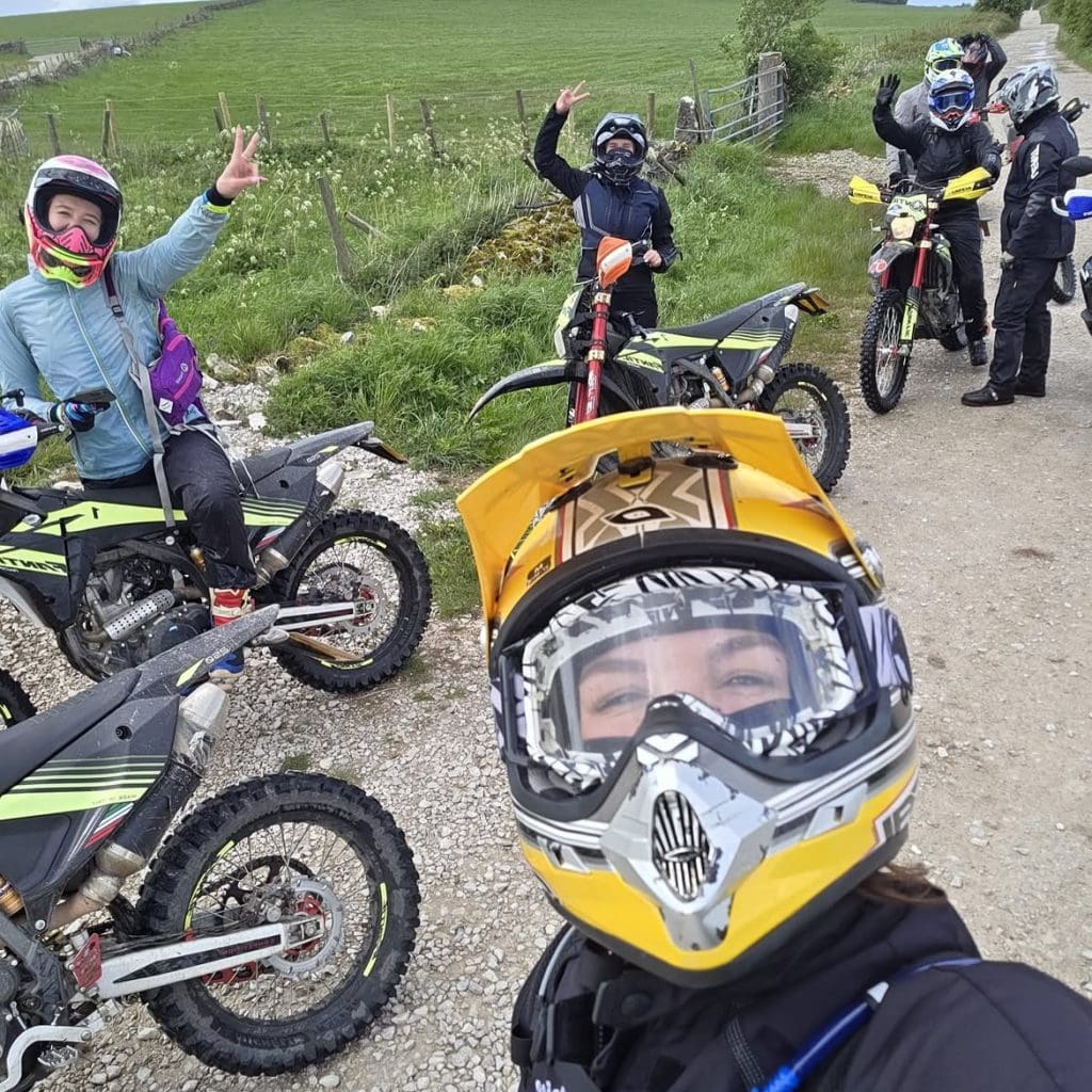 Selfie from a trail rider in a yellow motorcycle helmet showing three dirt bike motorcyclist in the background waving for the camera